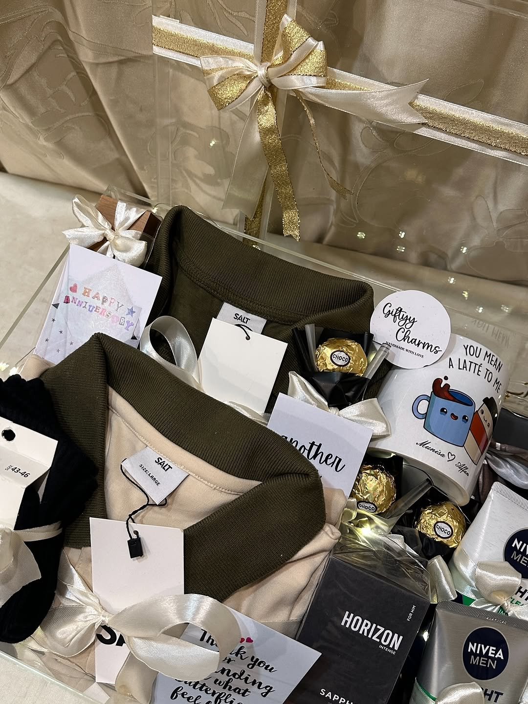 ๐ 2 stylish T-shirts / polo shirts โ olive green & beige ๐งด Horizon Intense perfume ๐งด NIVEA MEN body care product โ Cute printed coffee mug ๐ซ Ferrero Rocher-style chocolates ๐ Birthday & cute message cards ๐ White/golden decorative ribbons ๐ก Fairy lights ๐ Premium transparent gift hamper box